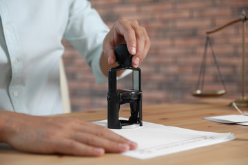 Male notary stamping document at table, closeup. Space for text