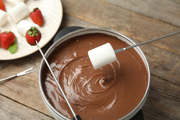 Dipping marshmallow into pot with tasty chocolate fondue on table