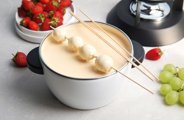 Pot with white chocolate fondue, dipped grapes and sticks on table