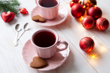 Christmas holiday background with two cups of tea and cookies, red Christmas balls and garland on white vintage wooden background. Close-up, selective focus.  Christmas and New Year concept