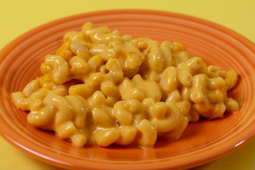 Close up of kid's style macaroni and cheese on an orange plate with a yellow background.