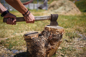 A strong man's hand with an axe chopping wood at a camping in a mountainous region of Georgia. The muscles on the hand and bracelets, a stump with an axe.