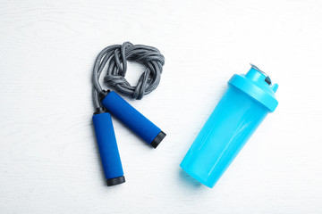 Jump rope and bottle of water on white wooden background, top view