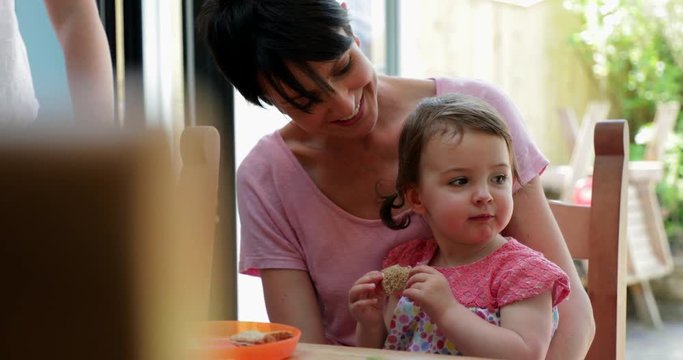 Little Girl Sitting on Her Mothers Lap Trying New Foods