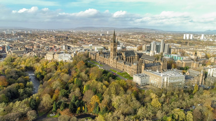 Low level aerial image over the autumn foliage of trees in Kelvingrove Park, Glasgow, to the gothic tower of Glasgow University with the cityscape behind.