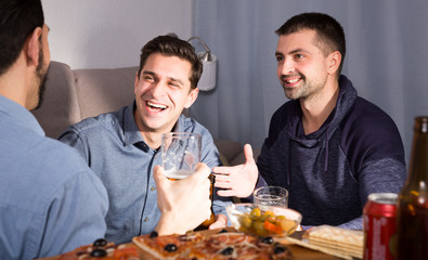 Happy males talking over beer with pizza at home