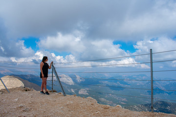 back view of young woman dressed black with dark hair standing on top of Tahtali Mountain in Kemer, Turkey and enjoy the View. 