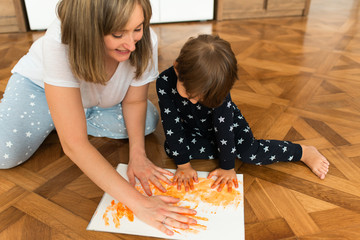 Happy mother and kid playing together and smiling in the living room, sitting on the floor and...