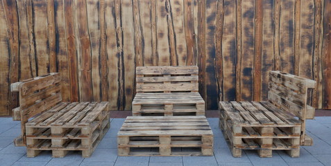 Rustic, self-made benches and a table made of euro pallets in front of a wooden wall
 