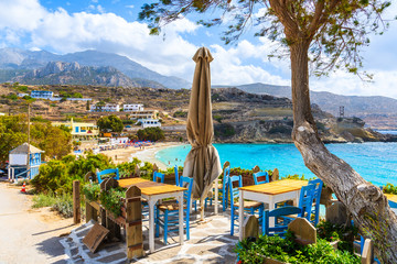 Taverna tables on terrace and view of beautiful beach in Lefkos village on coast of Karpathos island, Greece
