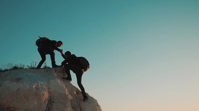 Teamwork friendship hiking help each other trust assistance silhouette in mountains. Backpacker helps to his friend to climb to rock. two travelers help stretching hand tourist lifestyle concept