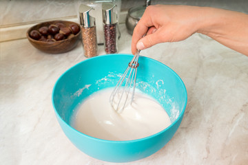 Girl in the kitchen preparing stainless balloon whisk batter for frying pancakes in a turquoise bowl