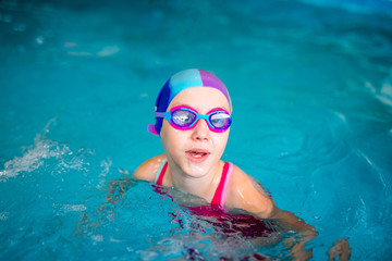 Fototapeta na wymiar Happy girl with swimming hat and glasses in the blue pool indoor