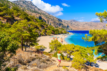Young woman tourist walking on cliff path to beautiful Apella beach on Karpathos island, Greece