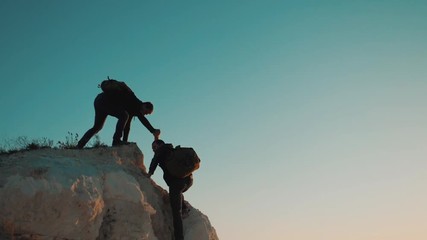 Teamwork friendship hiking help each other trust assistance silhouette in mountains. Backpacker helps to his friend to climb to rock. two travelers help stretching hand lifestyle tourist concept