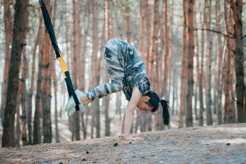 young attractive woman doingexercise training core using trx suspension straps in the forest