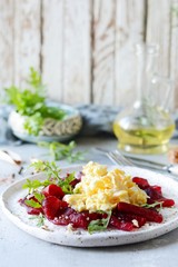 Scramble of eggs with carpaccio of baked beets with walnuts, aromatic herbs and arugula on a plate. Delicious healthy breakfast.  Beet carpaccio with sauce on a white plate.