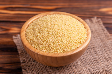 Raw couscous grain in wooden bowl with burlap napkin