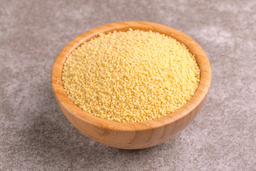 Raw couscous grain in wooden bowl on gray marble background