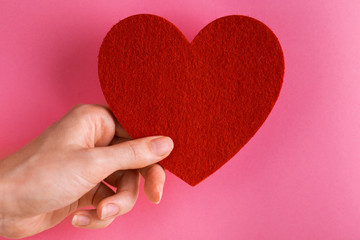 Red felt heart in woman's hand on bright pink background