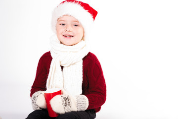 Merry Christmas and happy New year! Cute happy little boy holding red cup. Kid enjoy holiday santa hat. Portrait kid on light background isolated. Happy Child with place for text