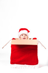 Merry Christmas and happy New year! Cute happy little boy sit in big christmas box with gift bag. Kid enjoy holiday in santa claus coat on light background. Happy Child with place for text.