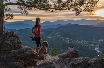 A hispanic woman is hiking with a dog, at sunset, in the Rocky Mountains near Denver, Colorado, USA