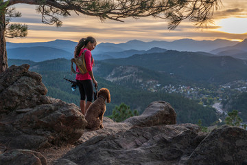 A hispanic woman is hiking with a dog, at sunset, in the Rocky Mountains near Denver, Colorado, USA