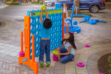Sister watches younger brother struggle to insert a large wring in a mega connect four game.