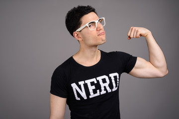 Young handsome nerd man with eyeglasses against gray background