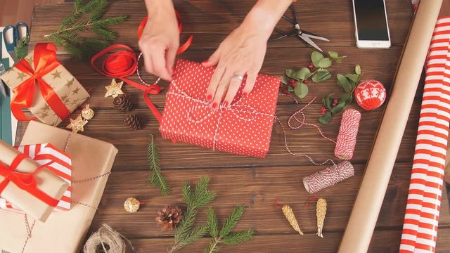 Christmas flat lay of unready hand crafted gift box on rustic wooden table with rolls of craft and colour wrapping paper, pine cones, fir branches and decor elements.