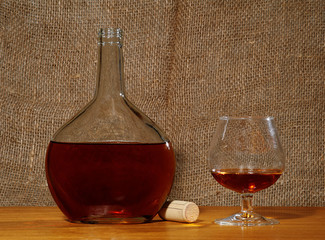 Bottle and wineglass with cognac on the table with canvas background