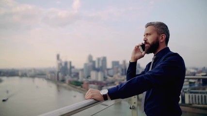 A portrait of businessman with smartphone standing against London view panorama. - Powered by Adobe