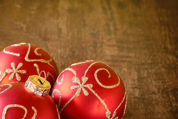 Close-up of three mat red christmas balls with golden swirly decoration on old dark teak table with copy space for use as a christmas background or christmas card  