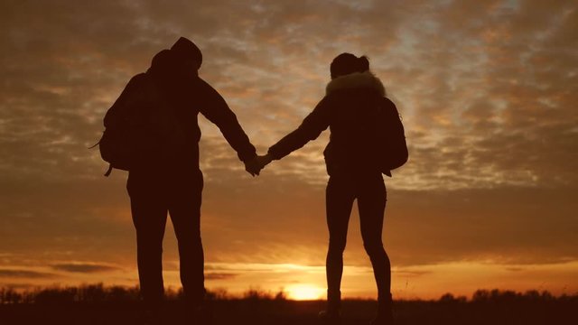 Silhouettes of two hikers with backpacks enjoying sunset view from top of a mountain. Enjoying the sunset view from mountain top above the clouds. Happy couple winner mountain top concept.