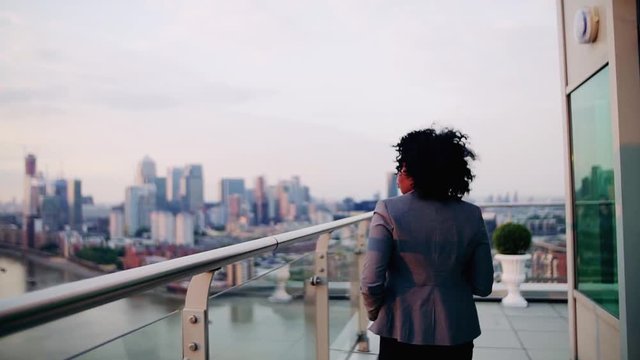 A rear view of businesswoman walking on a terrace at sunset.
