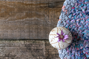 One lilac flower Xeranthemum on round clay vase on knitted patchwork and gray wooden background texture background. Wabi Sabi, Hygge, Lagom style. Loneliness, simplicity, minimalism still life concept
