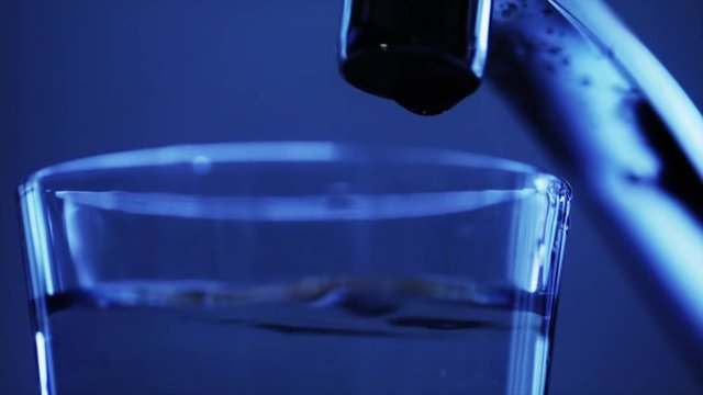 Water dripping in slow-motion from a kitchen tap. Blue tinted. Close up.