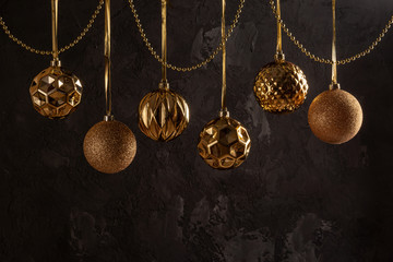 Fototapeta na wymiar Six beautiful golden Christmas balls hanging on a dark background. Below is a place for text.