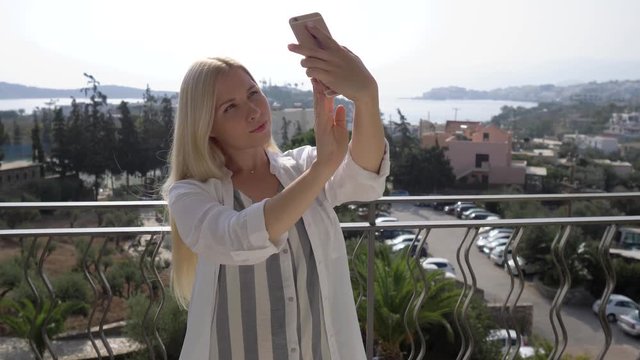 Young beautiful girl taking pictures of herself on the hotel terrace. The girl takes a selfie on the terrace. 4K