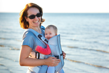 Baby and mother on sea at summer day. Child in a carrier backpack