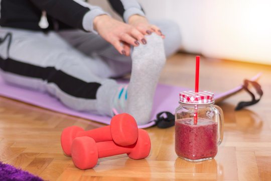 Dumbbell and smoothie in retro jar on floor and woman working stretching exercises legs in background at morning on yoga mat. Health life and food concept. Close up, selective focus