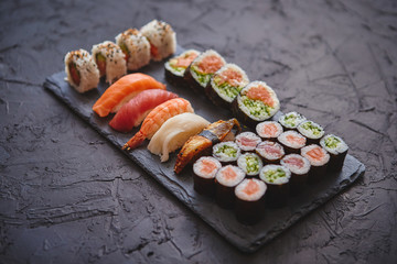 Fresh sushi rolls set with salmon and tuna fish served on black stone board. Top view of traditional japanese cuisine.