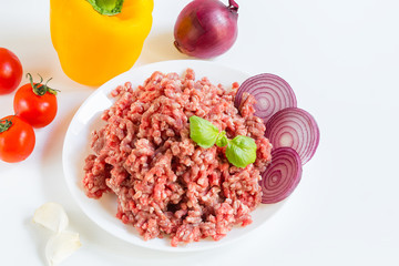 fresh raw minced beef in a white plate close up with pepper, onion and tomatoes, raw ingredients
