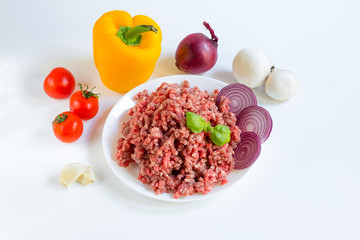 fresh raw minced beef in a white plate close up with pepper, onion and tomatoes, raw ingredients for stuffed peppers