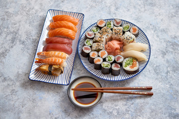 Asian food assortment. Various sushi rolls placed on ceramic oriental style plates. Soy souce and chopsticks on sides. Grungy dark background with copy space.