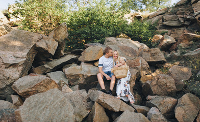 Young guy and cute girl hug sitting on the rocks. Beautiful love story of newlywed lovers.