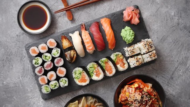 Japanese food composition. Various kinds of sushi placed on black stone board. Spicy kimchi salad, wontong soup, chopsticks and soy souce bowl.