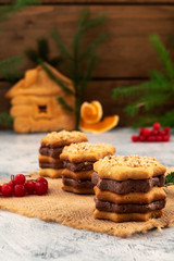 Cookies for Christmas with layers of chocolate filling, red berries of viburnum, branches of green spruce, wooden background, vertical.