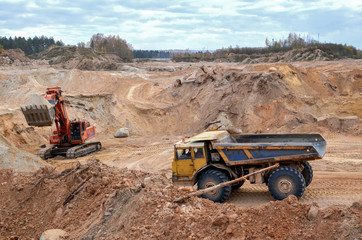 Excavator loading sand into dumper truck. Large quarry dump truck. View of the large sand pit. Production useful minerals. Mining.